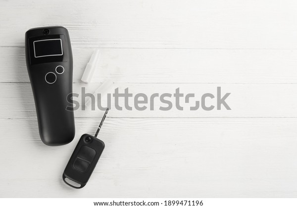 Modern breathalyzer, mouthpieces\
and car key on white wooden background, flat lay. Space for\
text