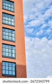 A modern brick building with large rectangular windows against a backdrop of blue sky and clouds. The architecture is minimalist in style, with part of the facade illuminated by sunlight.