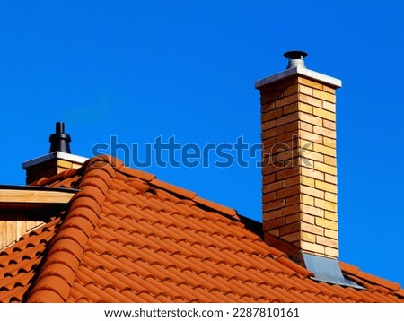 modern brick finished chimneys stack. concrete capping stone. brown red clay roof tiles. Zink plate chimney flashing. under blue sky. bright sunlight. metal flashing. construction concept