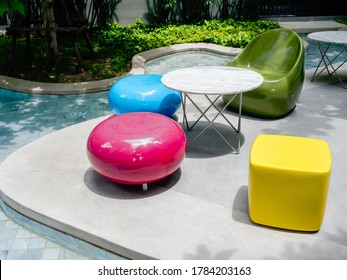 Modern Bright Colors Chairs And A Variety Of Shapes And Round Tables Beside The Outdoor Swimming Pool. Empty Colorful Furniture Decoration Near The Pool And Green Garden.