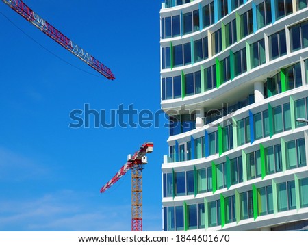 Modern building with blue and green colour windows construction detail and red colour tower cranes in front of blue sky in Budapest, Hungary