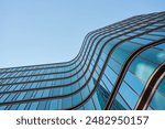 Modern building with curved glass facade reflecting sky. Contemporary architectural design against a clear blue backdrop