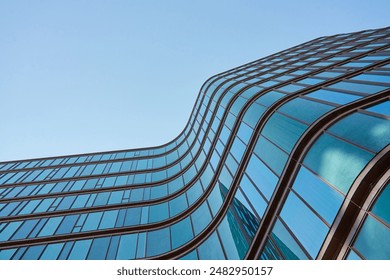 Modern building with curved glass facade reflecting sky. Contemporary architectural design against a clear blue backdrop - Powered by Shutterstock