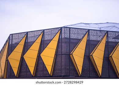 A modern building facade features geometric yellow panels, in an urban area, during the day, showcasing contemporary architecture through bold design and patterned structures.