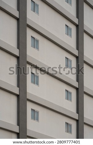Modern building facade featuring repeating rectangular windows and vertical structural columns in minimalist architectural style.