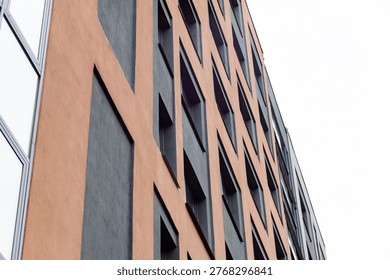 Modern building with geometric window patterns. Earth-toned facade contrasts with dark panels. Low-angle view emphasizes height and architectural rhythm