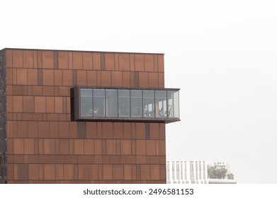 Modern building showcasing a unique architectural design with a glass balcony and rust-colored facade against a cloudy sky. - Powered by Shutterstock