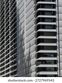 Modern building structure with unique window design showing shadows from nearby trees in bright sunlight