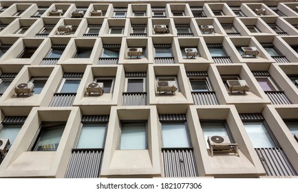A modern building with a yellow facade and lots of air conditioners. Many old air compressor at apartment building. Window a rectangular shape