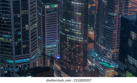 Modern Buildings With Blue Stained Glass Windows Glowing At Night In Dubai Media City Timelapse, United Arab Emirates. Aerial View From Above With Construction Site And Crane