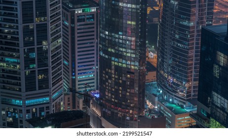 Modern Buildings With Blue Stained Glass Windows Glowing At Night In Dubai Media City Timelapse, United Arab Emirates. Aerial View From Above With Construction Site And Crane