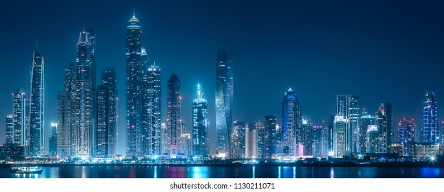 Modern buildings of Dubai Marina bay with lights at night on background, view from Palm Jumeirah, UAE - Shutterstock ID 1130211071