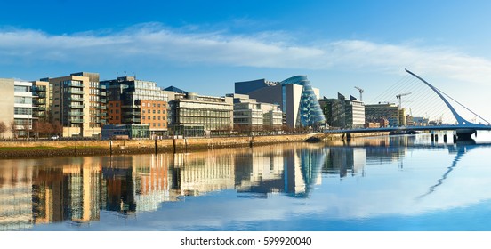 Modern buildings and offices on Liffey river in Dublin on a bright sunny day, bridge on the right is a famous Harp bridge.  - Shutterstock ID 599920040