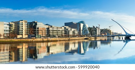 Modern buildings and offices on Liffey river in Dublin on a bright sunny day, bridge on the right is a famous Harp bridge. 