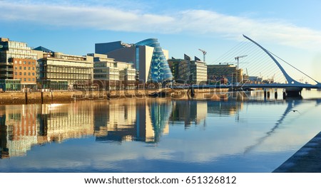 Modern buildings and offices on Liffey river in Dublin on a bright sunny day. Bridge on the right is a famous Harp bridge.