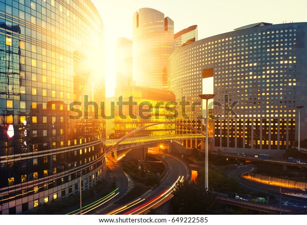 Modern buildings in Paris business district La\
Defense. Glass facade skyscrapers on a bright sunny day with\
sunbeams in the blue sky. Economy, finances, business activity and\
city traffic concept
