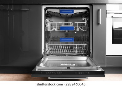 Modern built-in stainless steel dishwasher with open door in the kitchen front view. Household kitchen appliances. Dishwashing equipment.