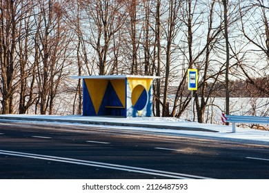 Modern Bus Shelter With Glass Design And Billboard Poster Holder Case In The Winter In Residential Urban Setting With Bare Trees, Salty Sidewalk, Wood Garbage Bin And Snowy Background. Polar Vortex.