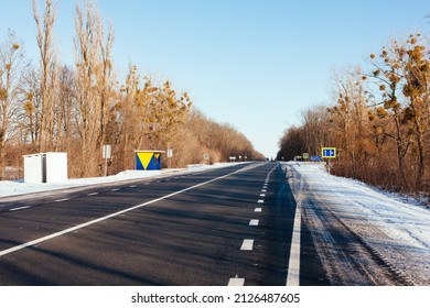 Modern Bus Shelter With Glass Design And Billboard Poster Holder Case In The Winter In Residential Urban Setting With Bare Trees, Salty Sidewalk, Wood Garbage Bin And Snowy Background. Polar Vortex.