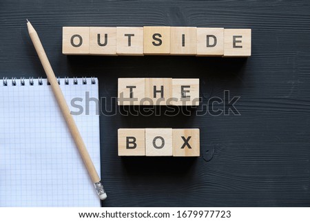 Modern business buzzword - Outside the Box. Top view on a black board, a notebook and pencil with wooden blocks. Close up. Top view.