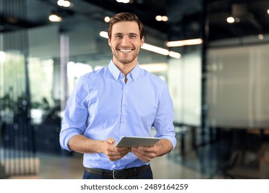 Modern business man in formalwear using digital tablet while standing near window in the office - Powered by Shutterstock