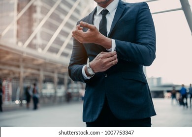 Modern Businessman. Confident Young Man In Full Suit Adjusting His Sleeve And Looking Away While Standing Outdoors With City  Background