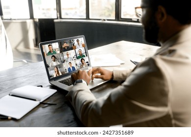 A modern businessman engages in a virtual meeting from his laptop in a bright, contemporary office space. The essence of remote work and the importance of connectivity in the corporate world - Powered by Shutterstock