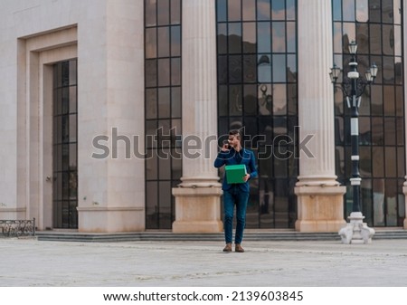 Modern businessman with notebook talking on cellphone at urban place against office buidling