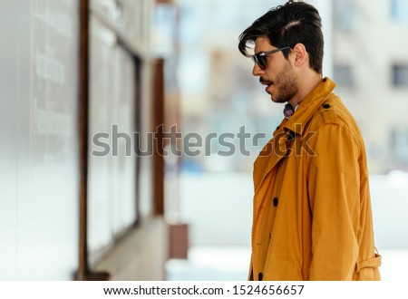 Modern businessman with yellow coat standing outdoors in down town and looking at the shop window, windowshopping