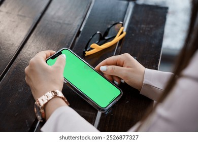 Modern Businesswoman Interacting with Smartphone Displaying Green Screen in Cozy Cafe Setting. - Powered by Shutterstock