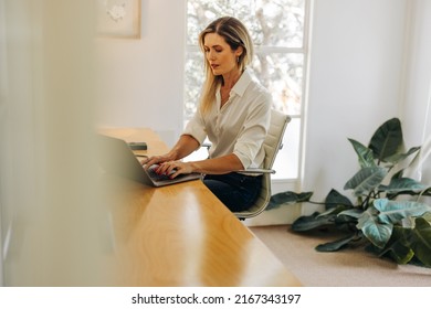 Modern Businesswoman Typing On A Laptop Keyboard While Sitting In Her Home Office. Young Businesswoman Writing An Email To Her Business Clients While Working From Home.