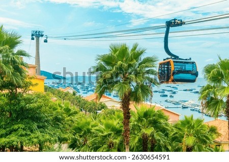 Modern cable car cabin gliding over lush palm trees with vibrant blue sea and boats in the background on Phu Quoc island, Vietnam at Sunset town. Modern tourism technology and infrastructure in Asia