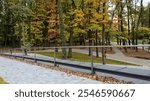 Modern cable railing with stainless steel posts and horizontal cables overlooks a park with colorful autumn trees and fallen leaves covering the paved path