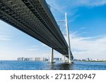Modern cable stayed bridge from low angle, sweeping over wide blue water with distant Saint Petersburg skyline on the horizon under a clear blue sky. Western High-Speed Diameter (ZSD) bridge