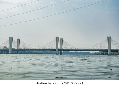 Modern cable-stayed bridge spanning the Hun River in Shenyang, China. Gray steel structure with distinctive towers reflected in calm water under clear sky.