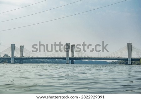Modern cable-stayed bridge spanning the Hun River in Shenyang, China. Gray steel structure with distinctive towers reflected in calm water under clear sky.