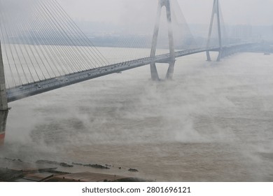 Modern cable-stayed bridge spanning the Yangtze River in dense fog, showcasing architectural engineering across the misty waters with dramatic atmospheric conditions.