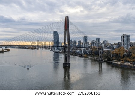 A modern cable-stayed bridge spans the Fraser River with a city skyline backdrop in Greater Vancouver, BC. Fraser River between Surrey and New Westminster, Greater Vancouver, BC, Canada.