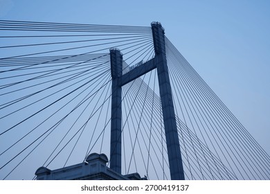 Modern cable-stayed bridge structure captured against a clear blue sky. Architectural engineering marvel with geometric symmetry and steel cables creating dynamic visual patterns.