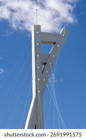 A modern cable-stayed bridge tower with angular design and tension cables stands against a vivid sky. The structure showcases contemporary engineering and geometric aesthetics.