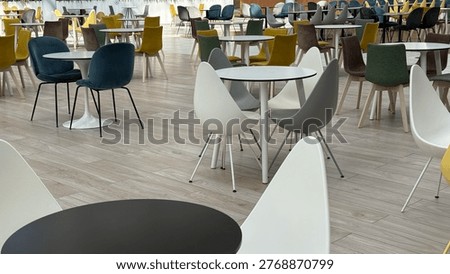 Modern cafeteria interior with empty tables and colorful chairs arranged on light wooden flooring. Mobile photo