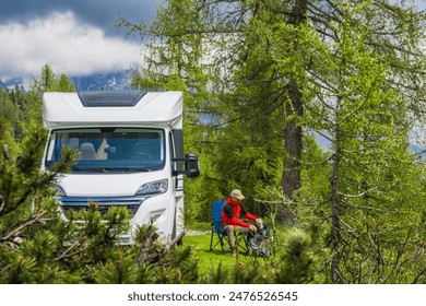 Modern camper van is parked in a mountain forest setting. A person is sitting in a camping chair near the van, presumably enjoying the scenery. RV Road trip. - Powered by Shutterstock