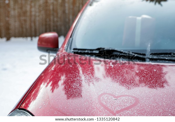 Modern car with drawn heart on hood in snowy\
winter forest, closeup. Space for\
text