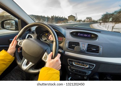 Modern Car Interior With Driver Female Hands On Steering Wheel, Winter Snowy Landscape Outside. Safe Driving Concept.