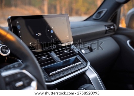 Modern car interior featuring a large floating touchscreen display with navigation, sleek air vents, and climate control buttons on a premium dashboard during sunset golden hour. High-tech cabin.