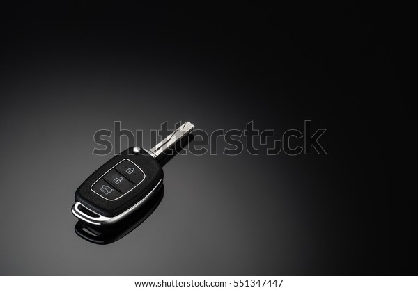 Modern car keys isolated on black\
reflective background with copy space for text or design elements.\
Folding key with remote alarm and trunk\
opening