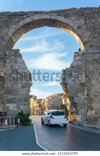modern car passes through the ancient Vespasian\
Gate in Side, Turkey