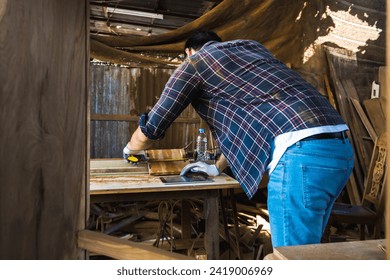 Modern carpenter using measuring tape measure piece of wood and looking at digital tablet while working with diy work in carpentry workshop
