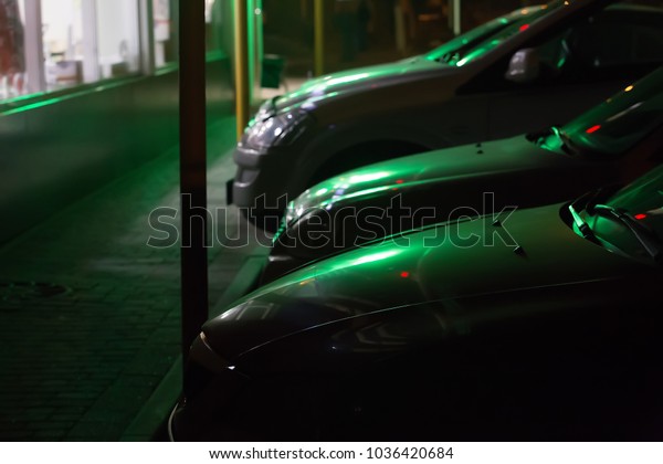 Modern cars lighted by green light of shop\
window parked close to\
pavement.