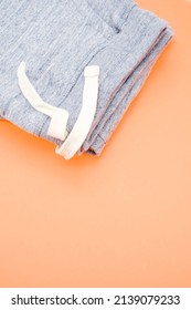 Modern Casual Apparels Concept - Pair Of Folded Denim Joggers With Laces On An Orange Table Viewed From Above